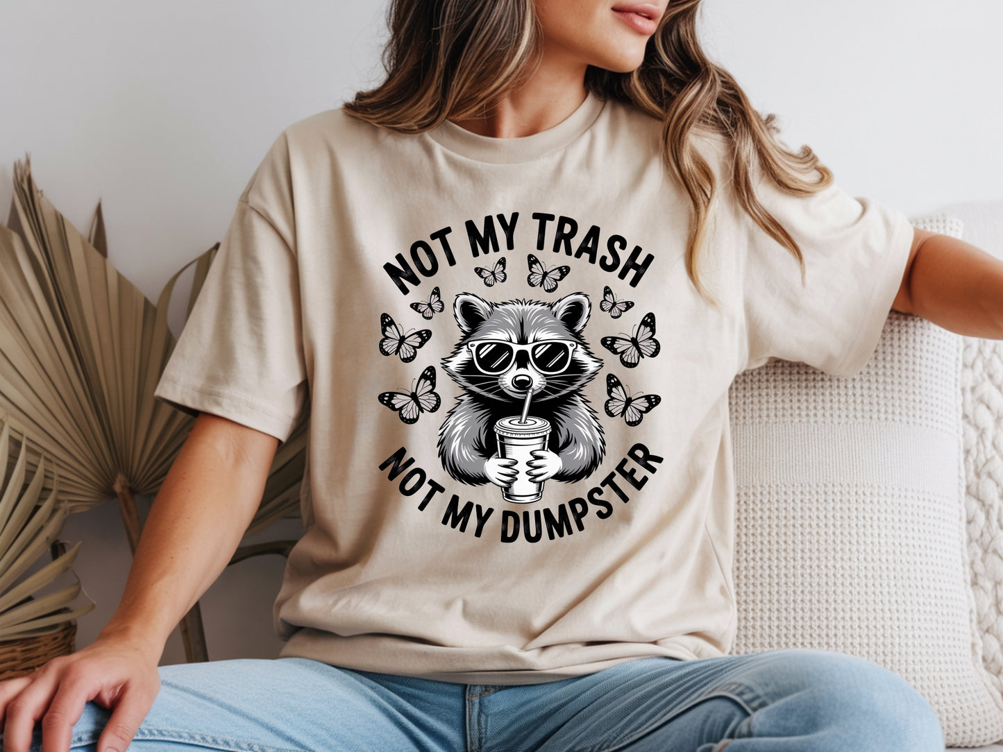 Beige raccoon shirt in oversized unisex fit featuring “Not My Trash Not My Dumpster” quote with a raccoon and butterflies. 