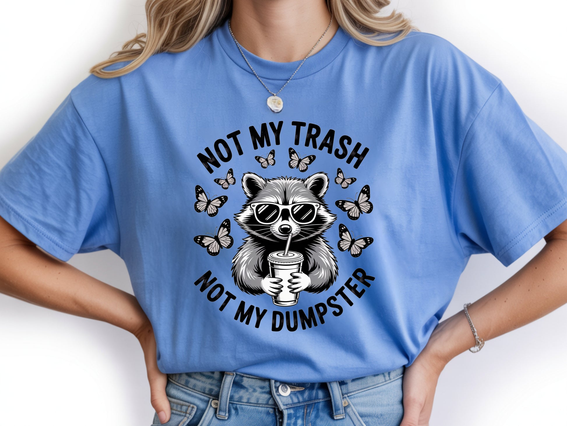 Blue raccoon shirt in oversized unisex fit featuring “Not My Trash Not My Dumpster” quote with a raccoon and butterflies. 