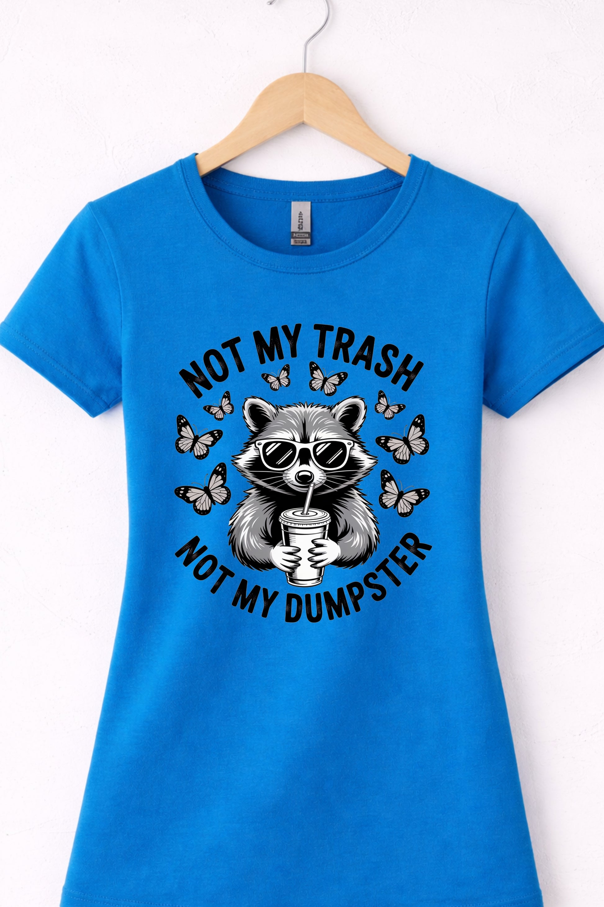Blue women’s crewneck raccoon shirt hanging flat with “Not My Trash Not My Dumpster” graphic.