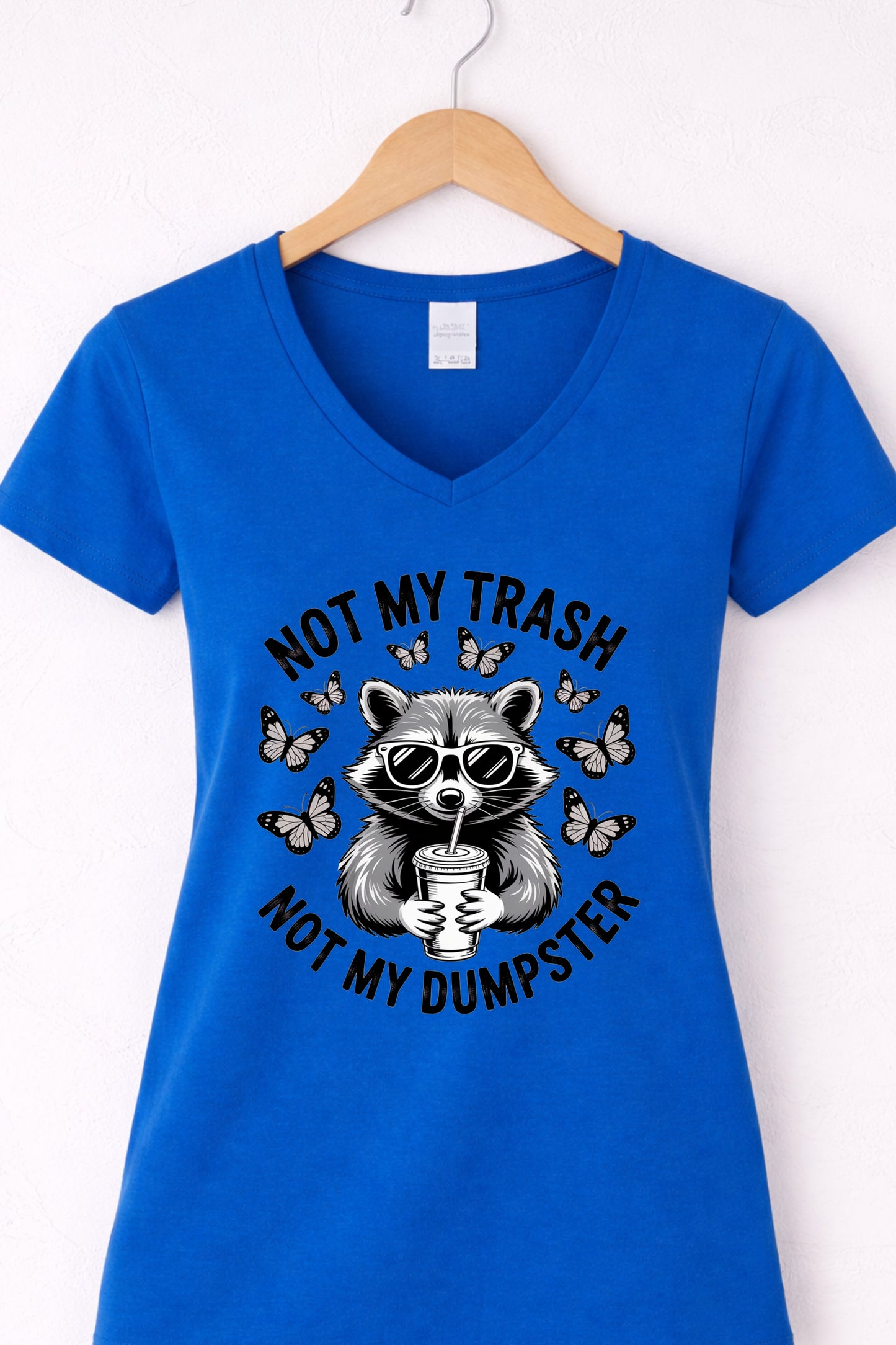 Blue women’s v-neck raccoon shirt hanging display featuring “Not My Trash Not My Dumpster” quote.
