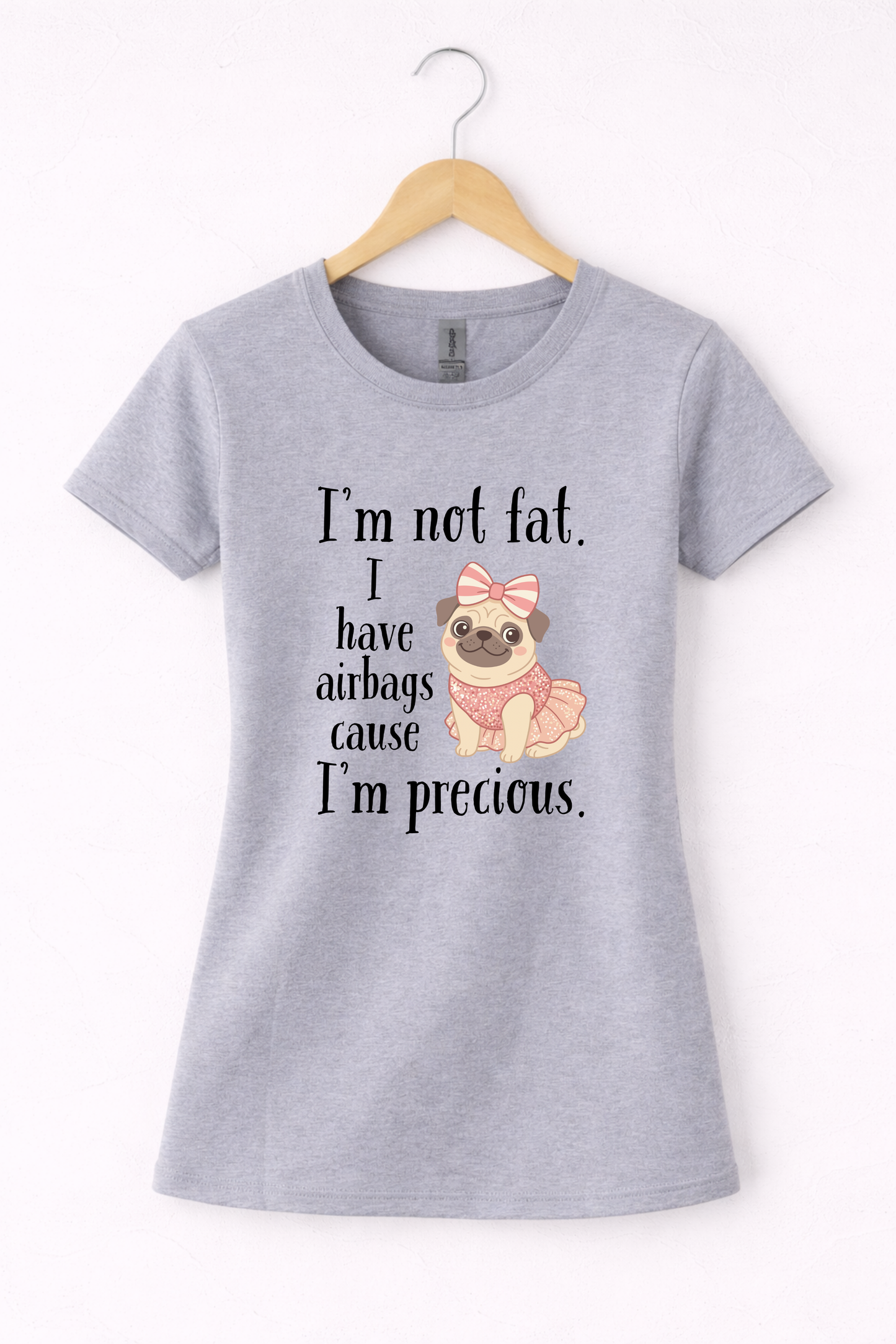 Grey women’s funny graphic crewneck t shirt hanging on wooden hanger featuring the “I’m Not Fat, I Have Airbags Cause I’m Precious” design.