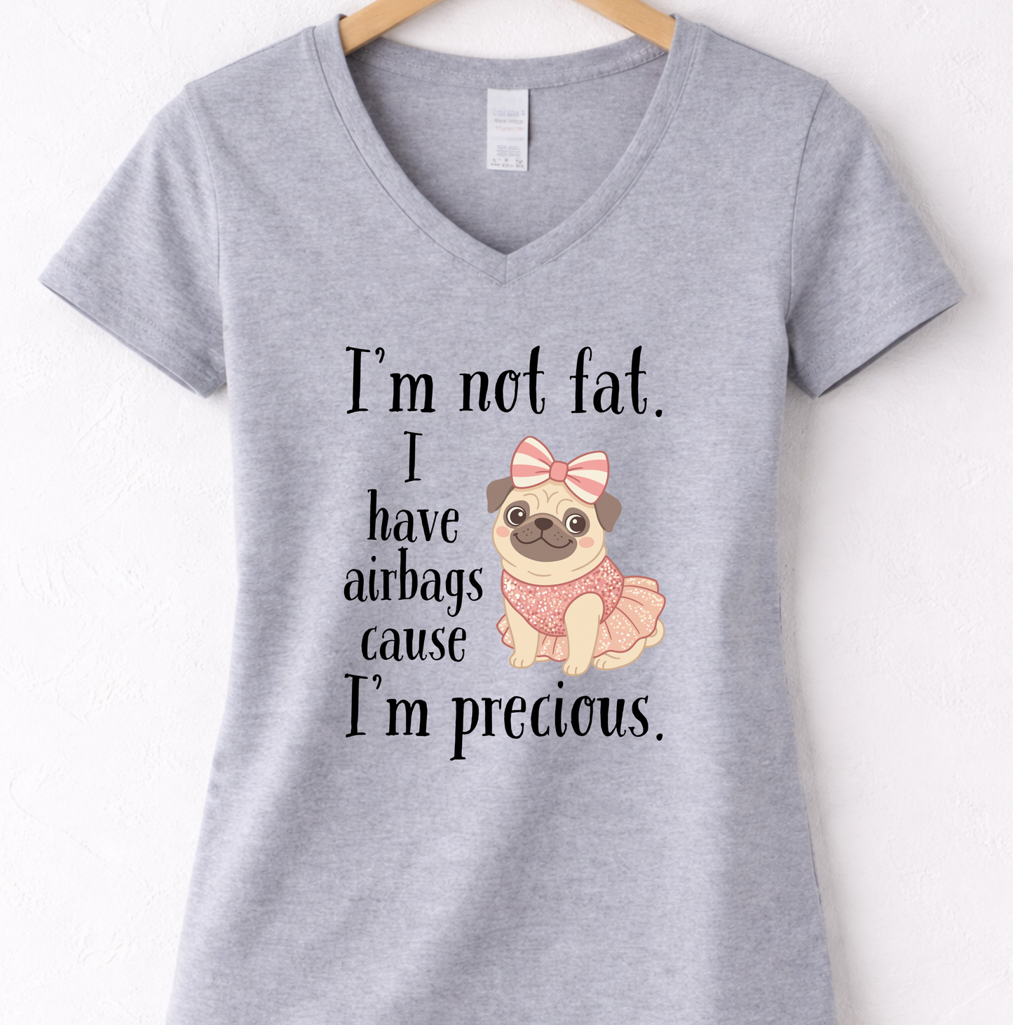 Grey women’s funny graphic V-neck t shirt hanging on wooden hanger with “I’m Not Fat, I Have Airbags Cause I’m Precious” quote.