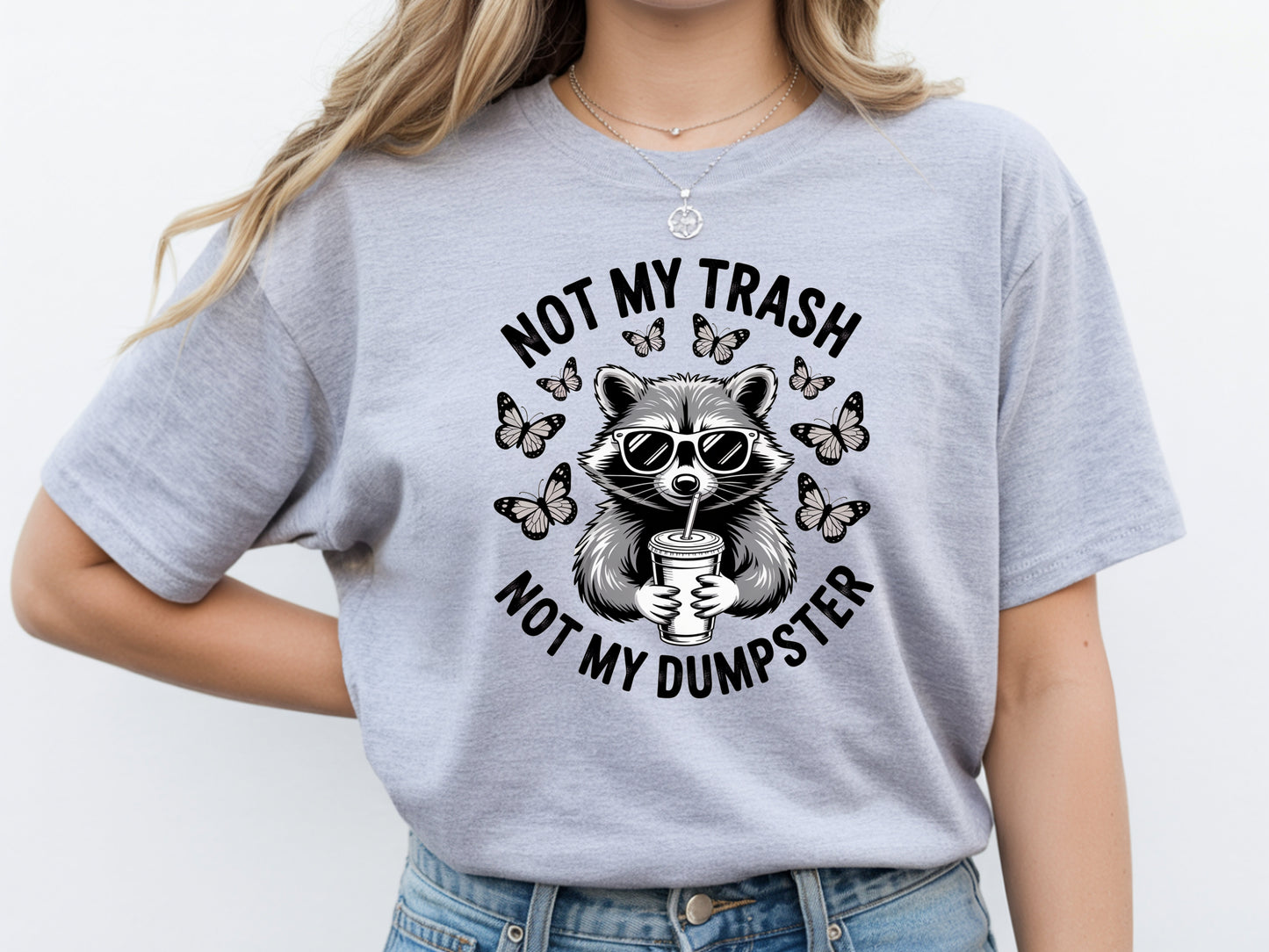 Grey raccoon shirt in oversized unisex fit featuring “Not My Trash Not My Dumpster” quote with a raccoon and butterflies. 