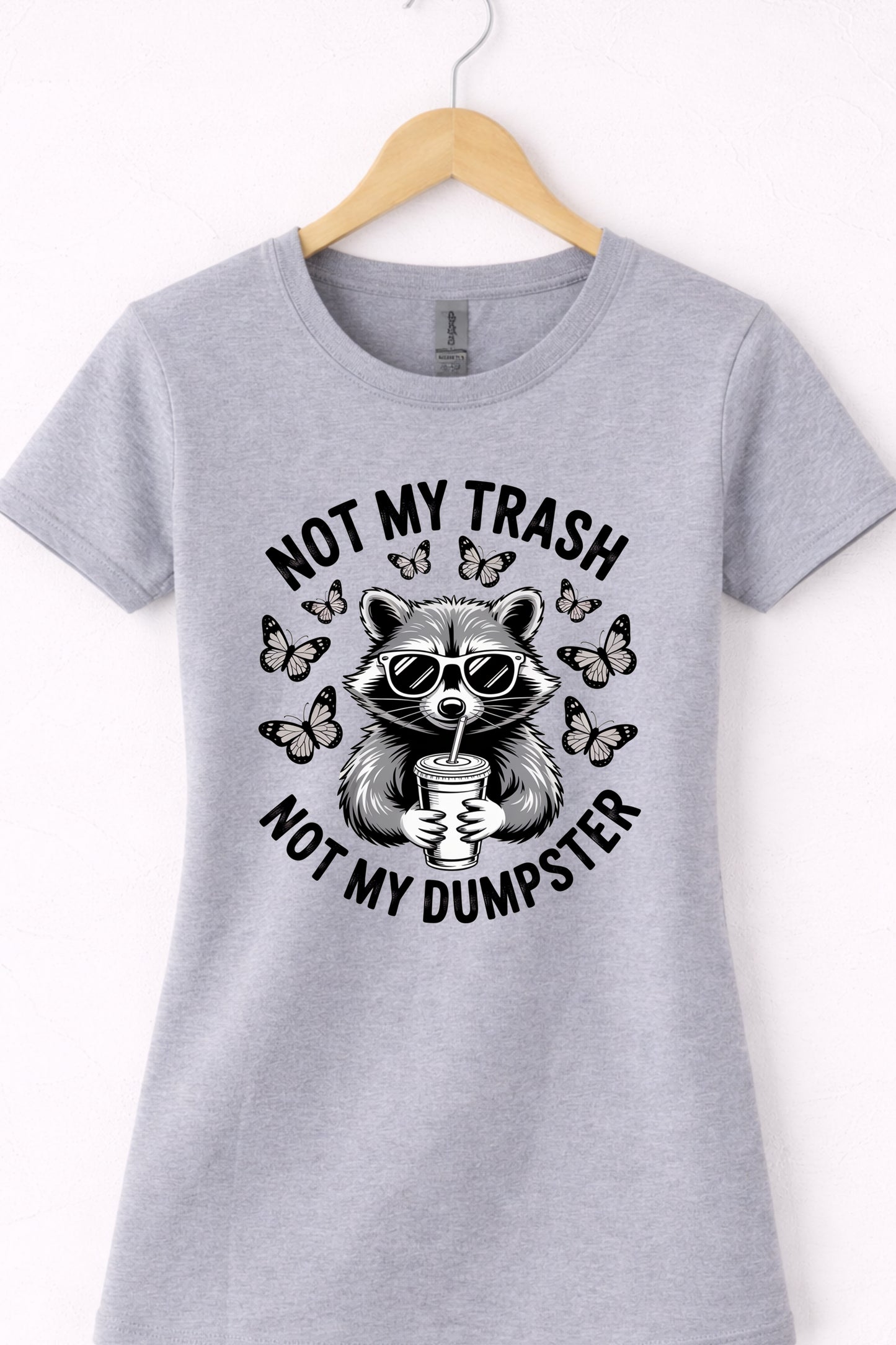 Grey women’s crewneck raccoon shirt hanging flat with “Not My Trash Not My Dumpster” graphic.