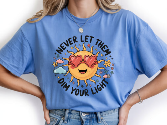 Never let them dim your light shirt with a cute sun graphic and "Never let them dim your light" text on a blue unisex shirt.