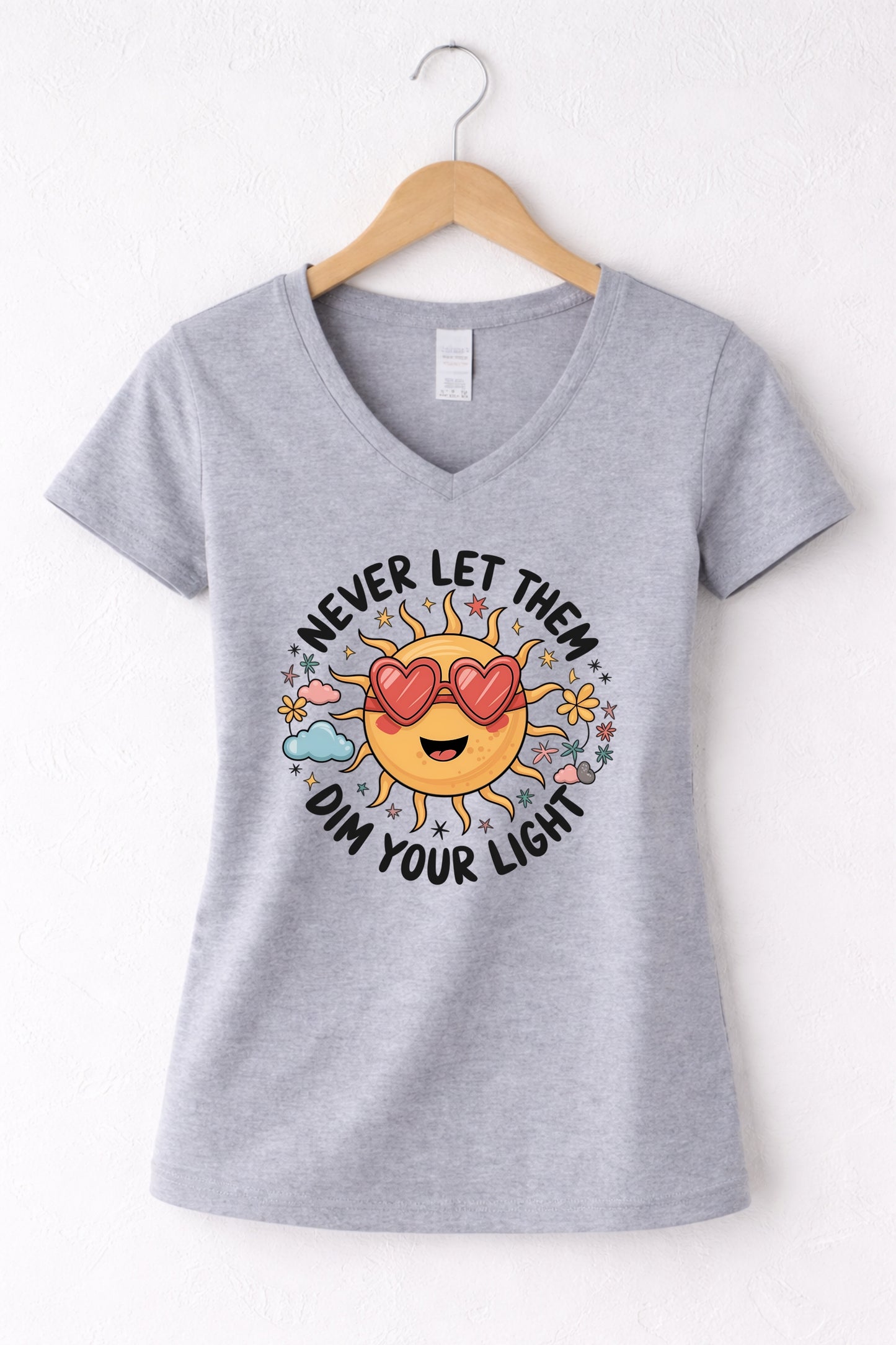 Never let them dim your light shirt with a cute sun graphic and "Never let them dim your light" text on a grey women's V-neck shirt.