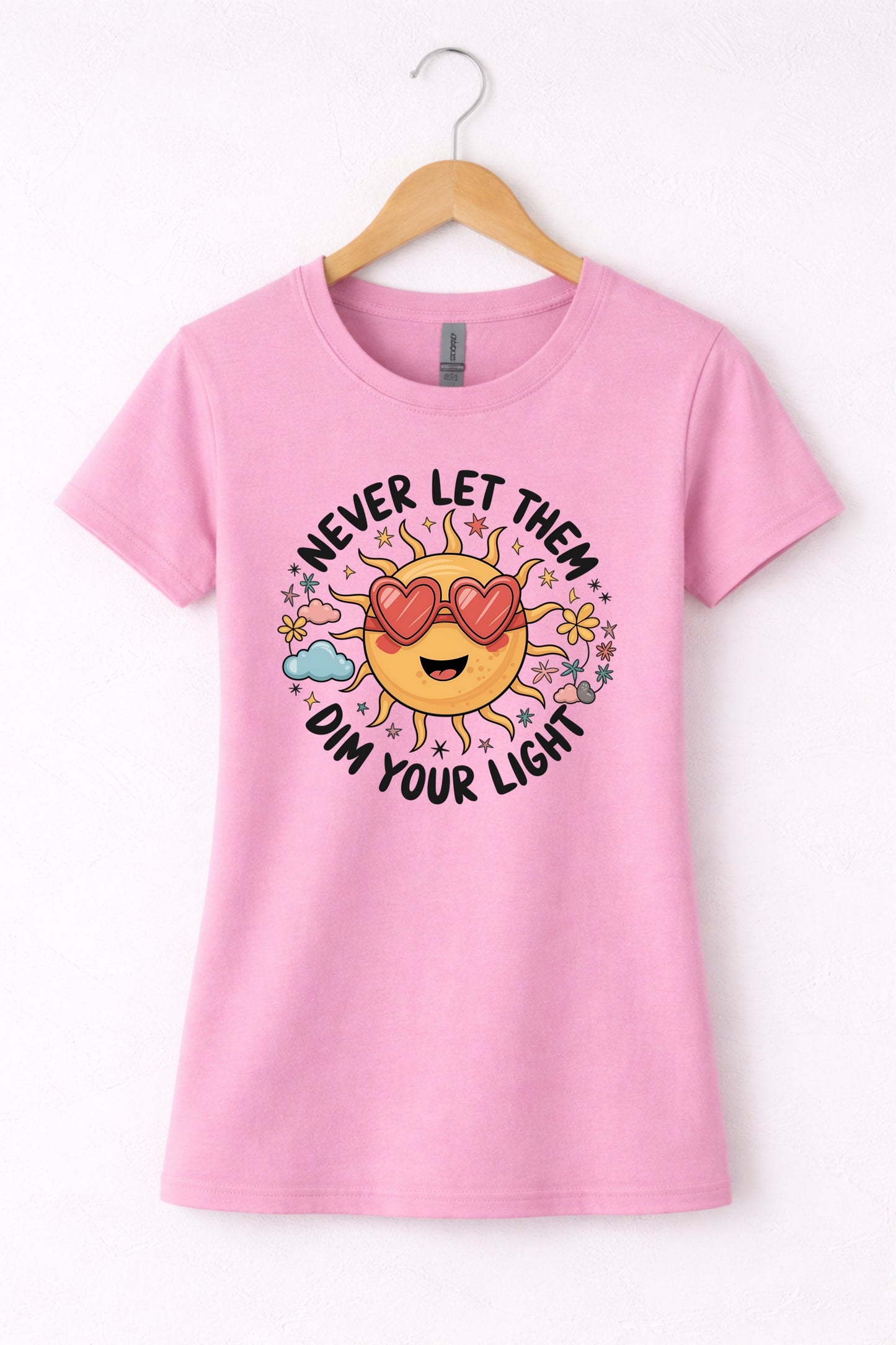 Never let them dim your light shirt with a cute sun graphic and "Never let them dim your light" text on a pink women's crewneck shirt.