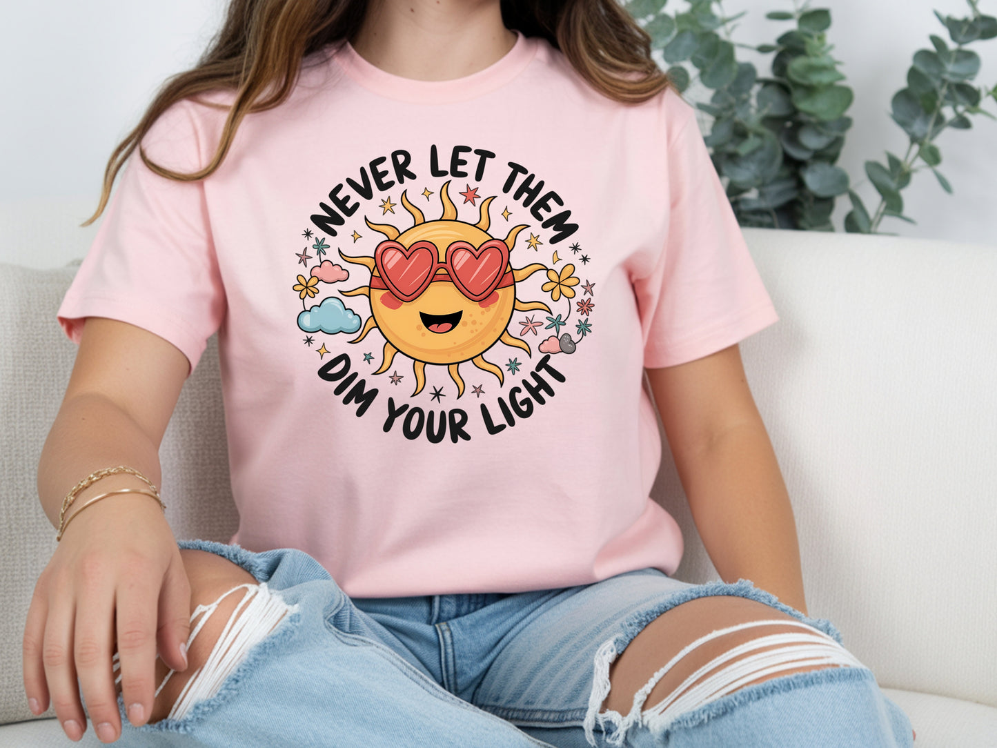Never let them dim your light shirt with a cute sun graphic and "Never let them dim your light" text on a pink unisex shirt.