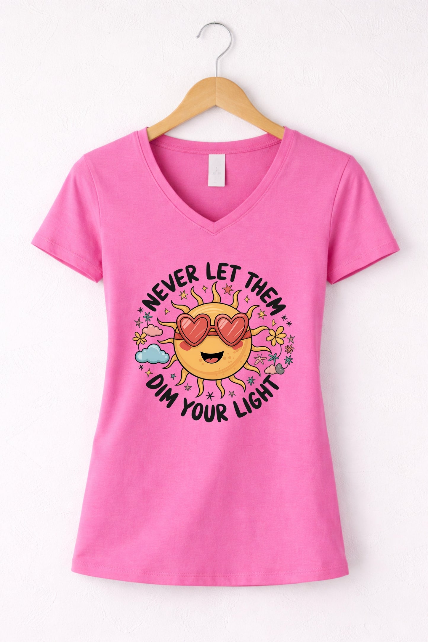 Never let them dim your light shirt with a cute sun graphic and "Never let them dim your light" text on a pink women's V-neck shirt.
