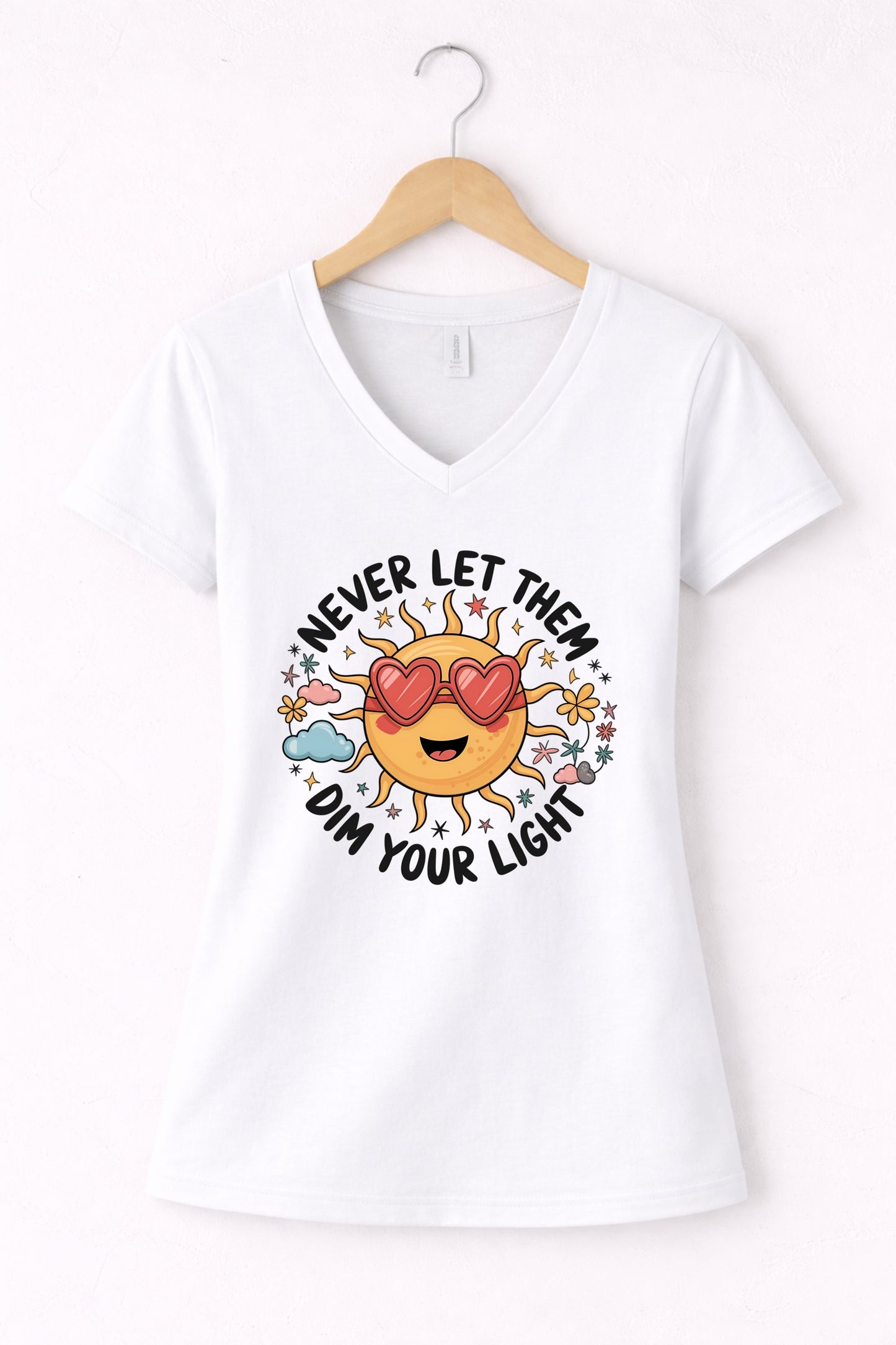 Never let them dim your light shirt with a cute sun graphic and "Never let them dim your light" text on a white women's V-neck shirt.