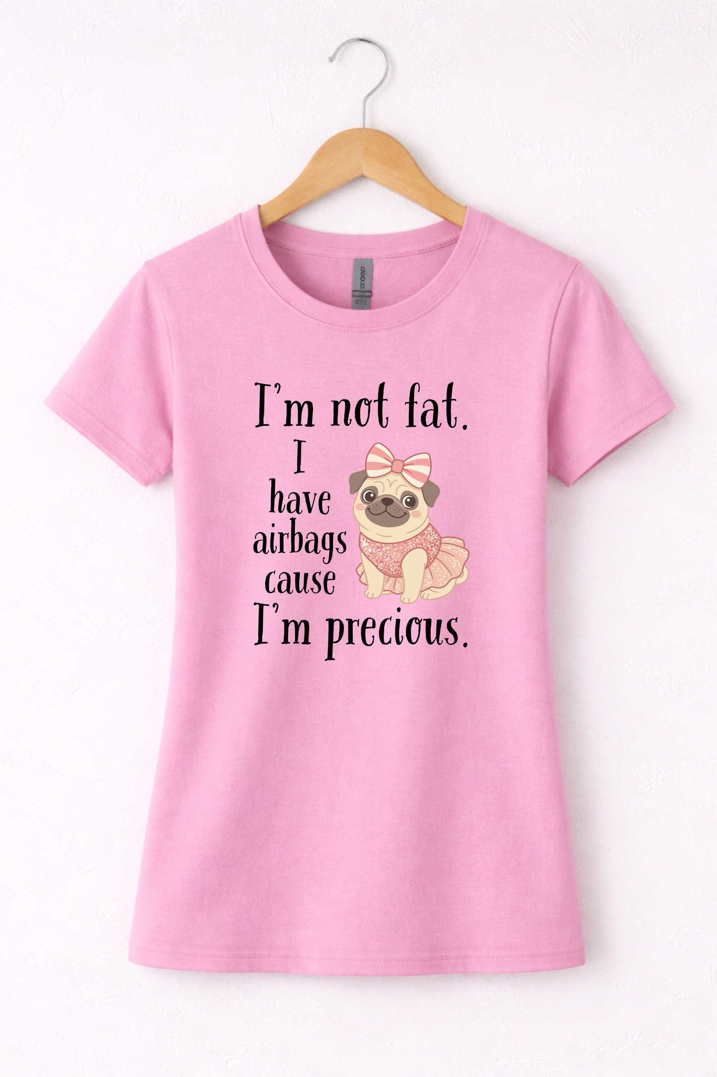 Pink women’s funny graphic crewneck t shirt hanging on wooden hanger featuring the “I’m Not Fat, I Have Airbags Cause I’m Precious” design.