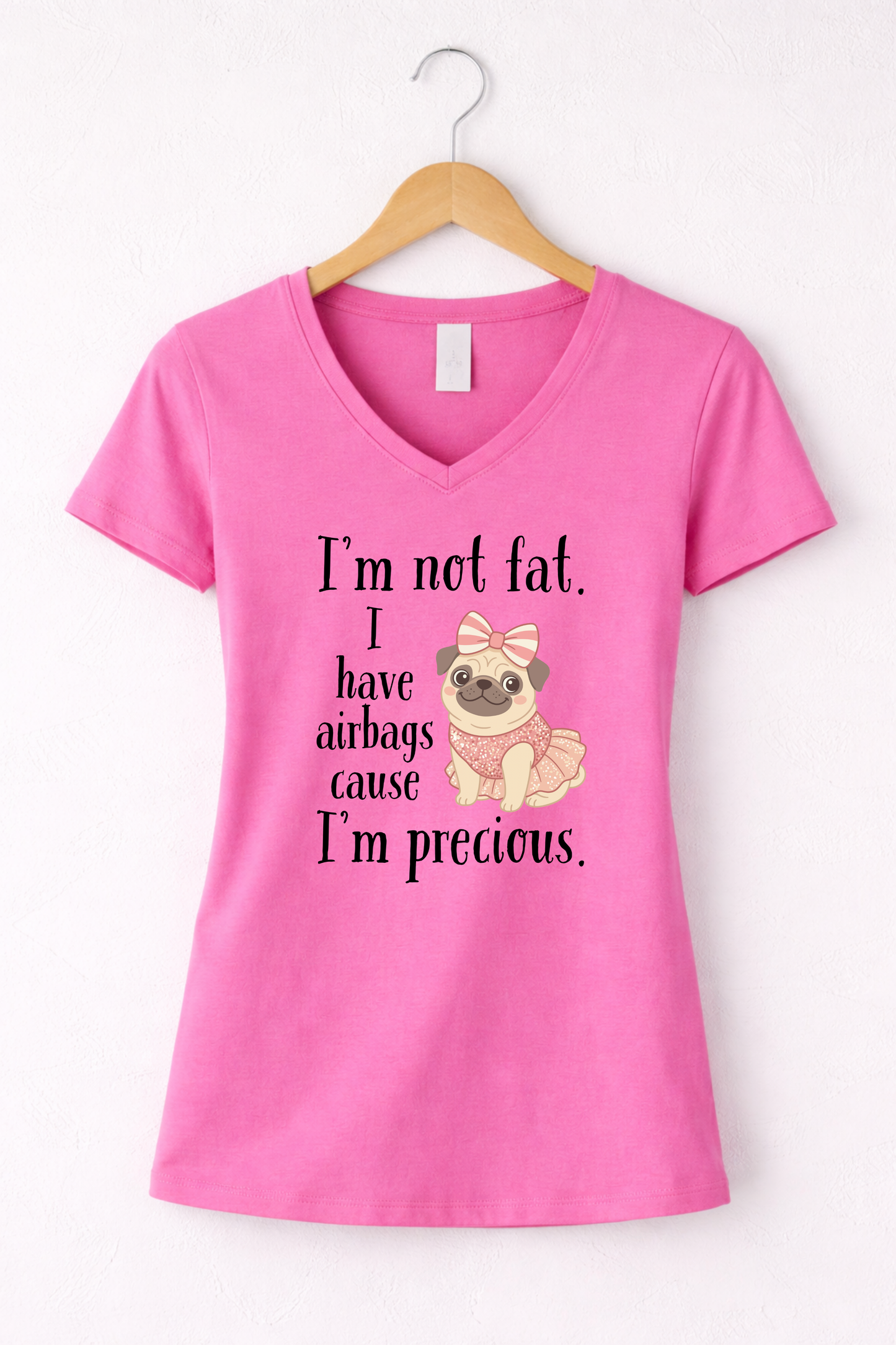 Pink women’s funny graphic V-neck t shirt hanging on wooden hanger with “I’m Not Fat, I Have Airbags Cause I’m Precious” quote.