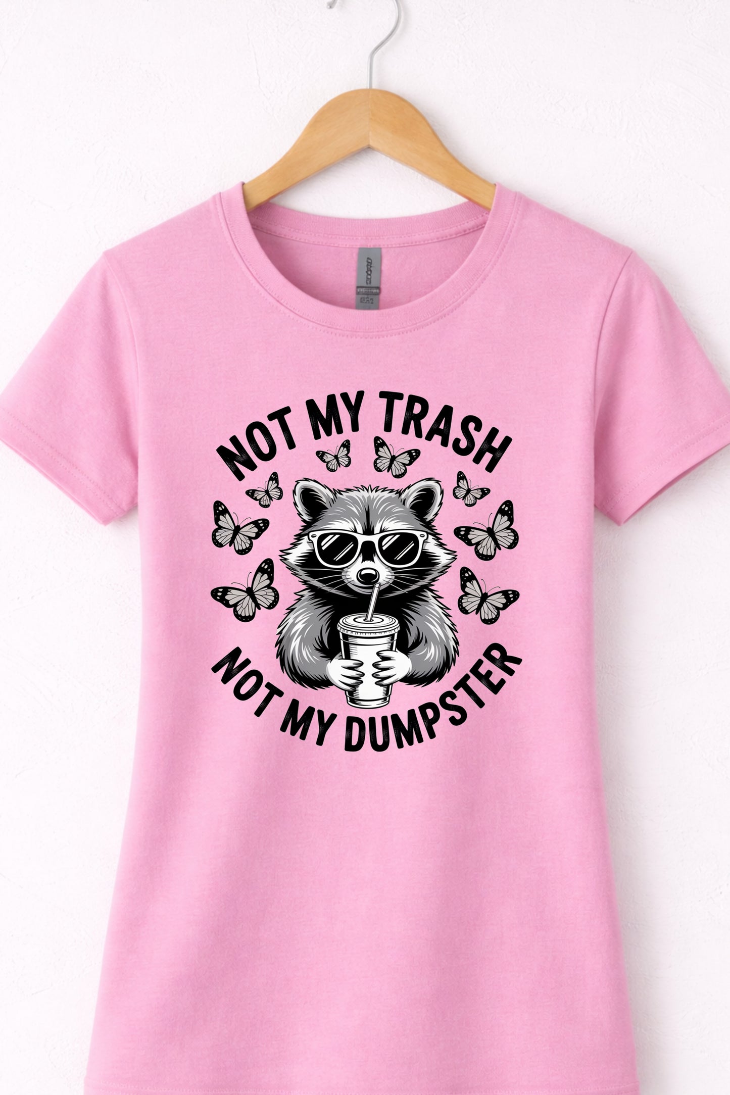 Pink women’s crewneck raccoon shirt hanging flat with “Not My Trash Not My Dumpster” graphic.