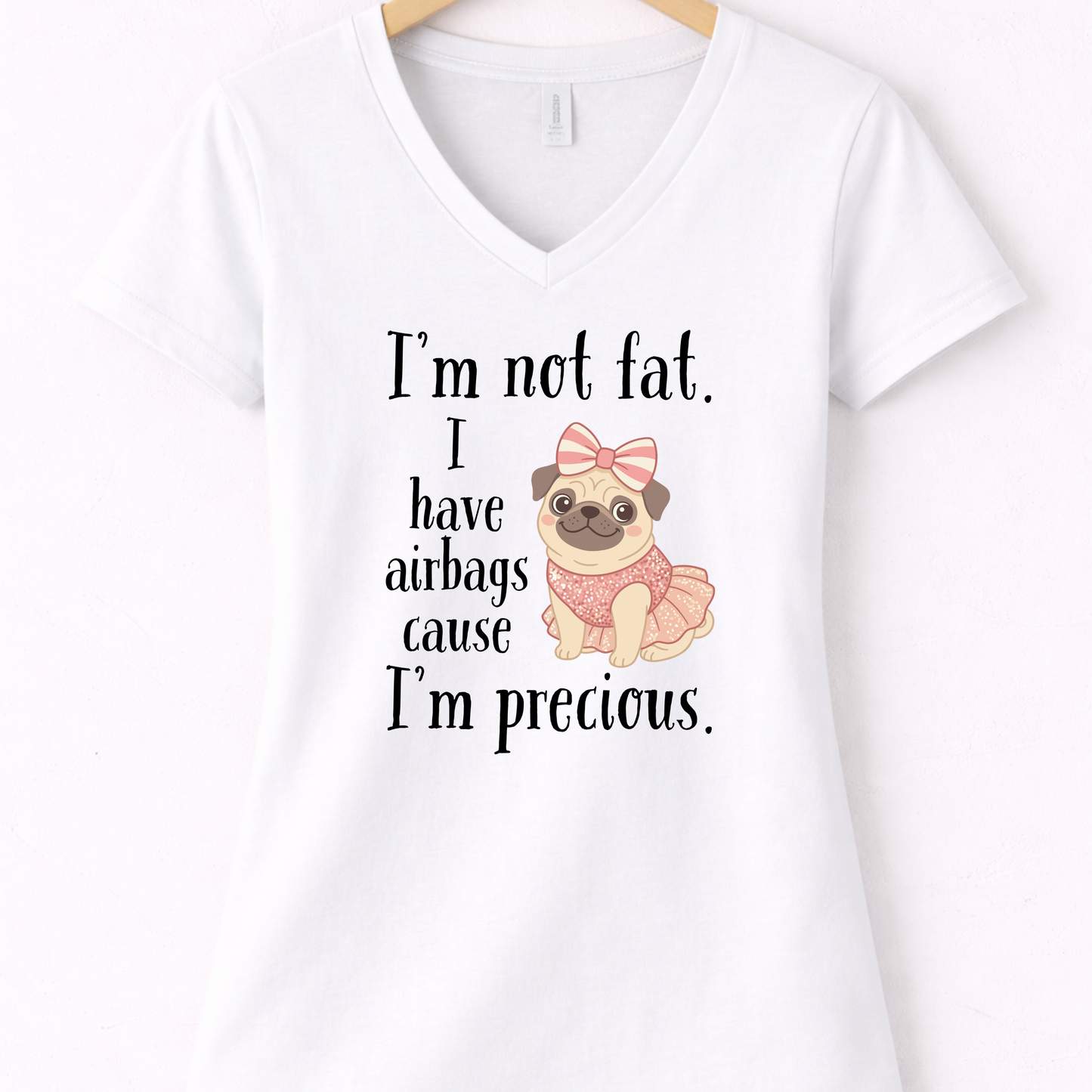 White women’s funny graphic V-neck t shirt hanging on wooden hanger with “I’m Not Fat, I Have Airbags Cause I’m Precious” quote.