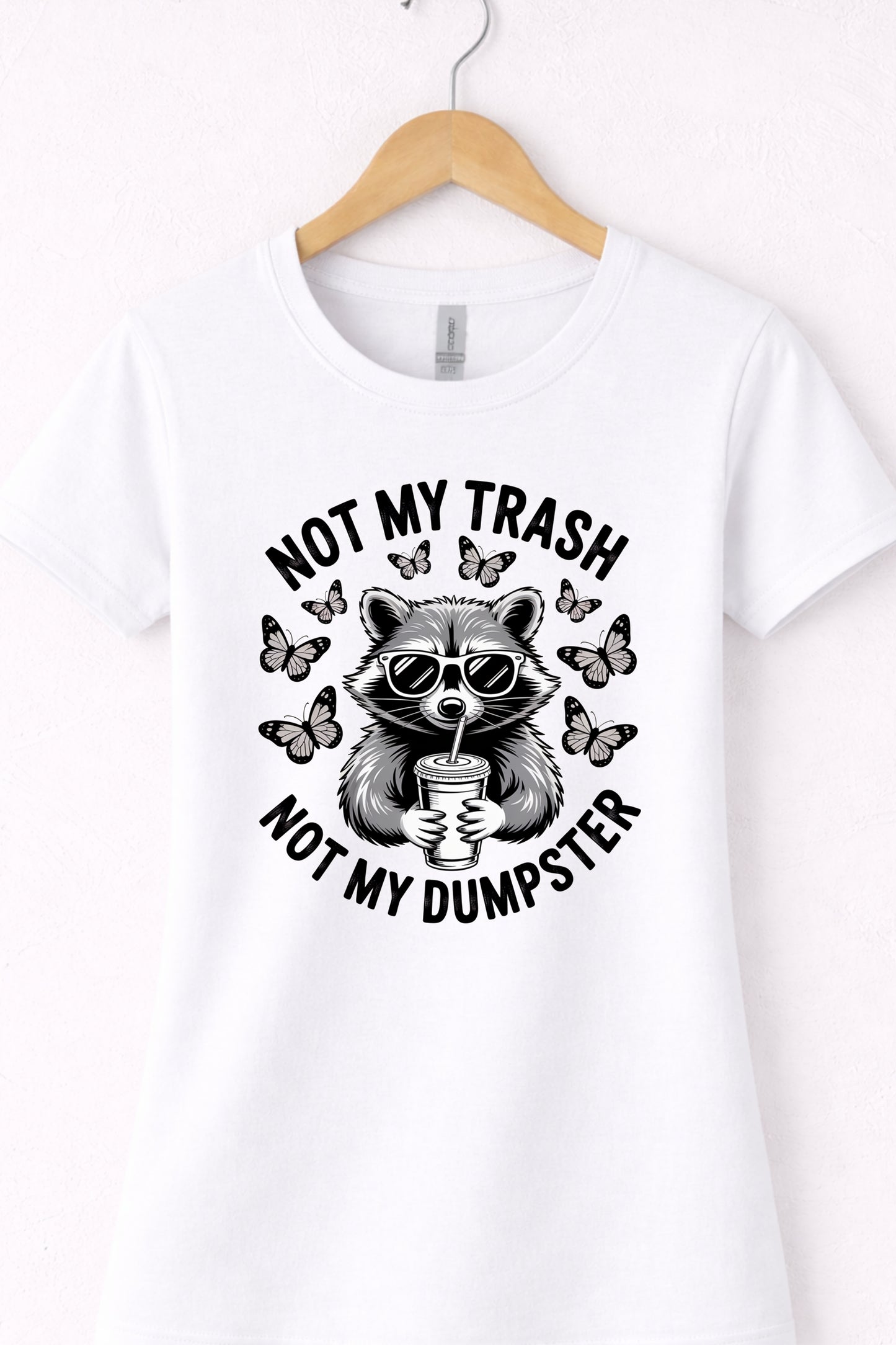 White women’s crewneck raccoon shirt hanging flat with “Not My Trash Not My Dumpster” graphic.