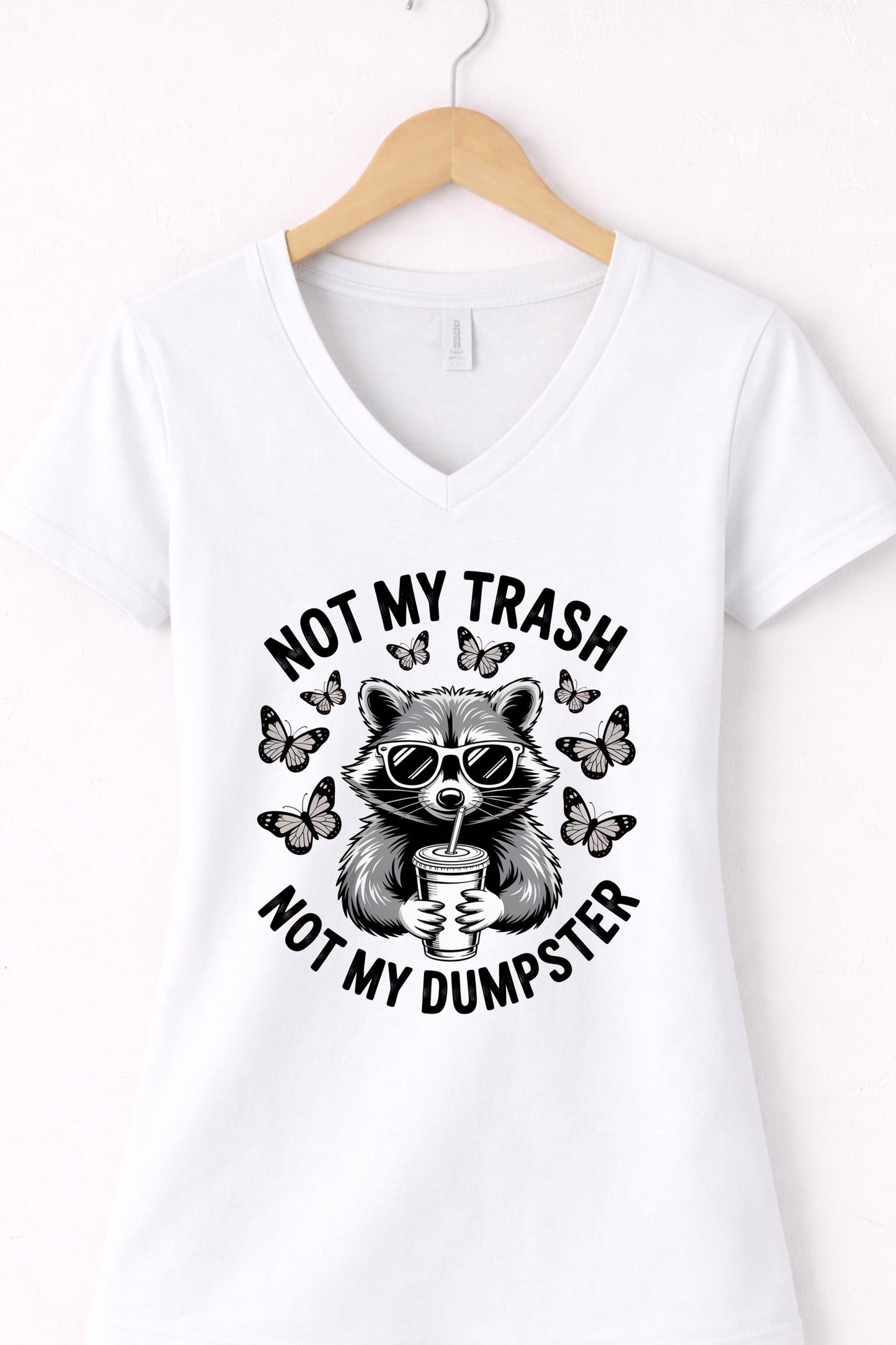 White women’s v-neck raccoon shirt hanging display featuring “Not My Trash Not My Dumpster” quote.