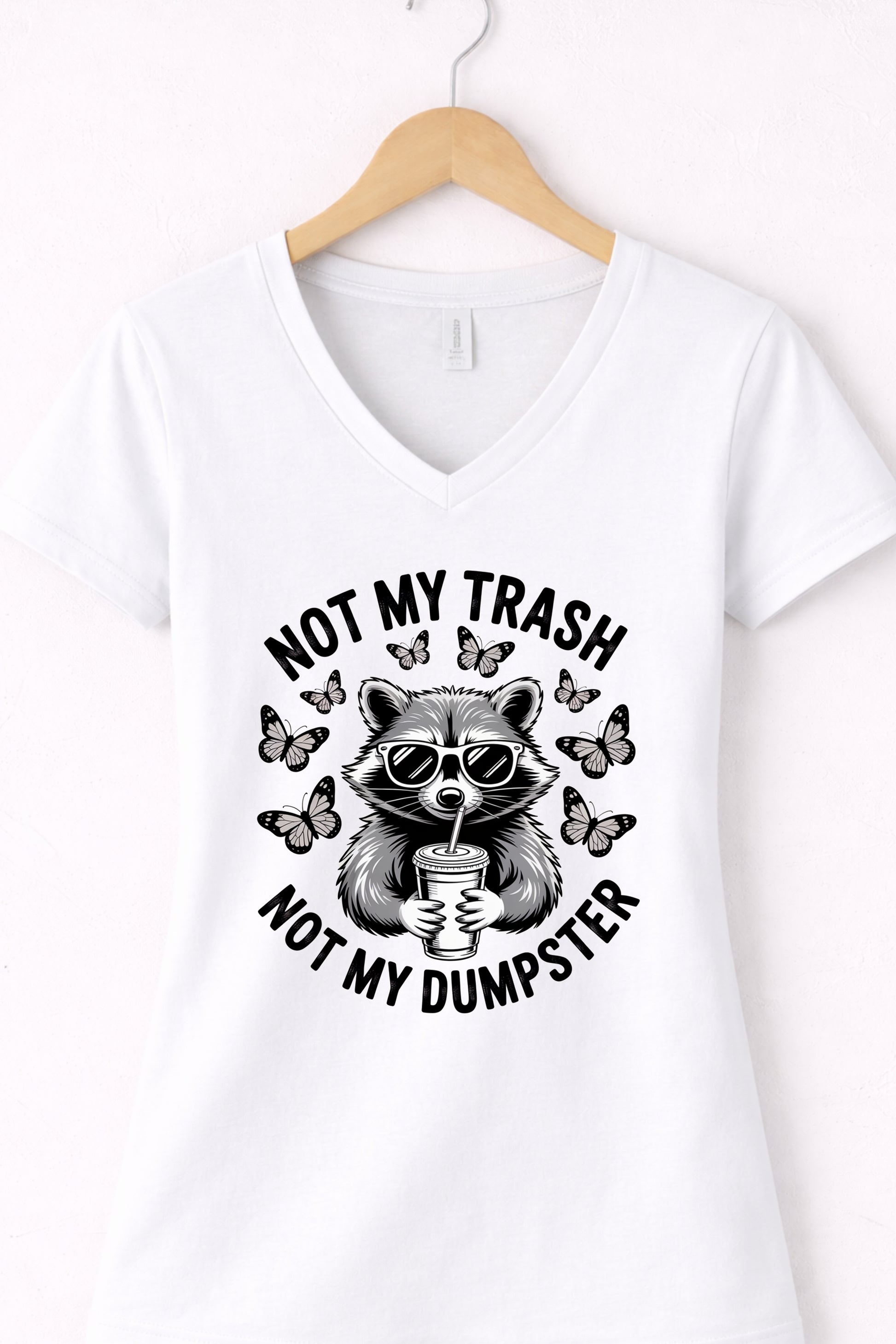 White women’s v-neck raccoon shirt hanging display featuring “Not My Trash Not My Dumpster” quote.